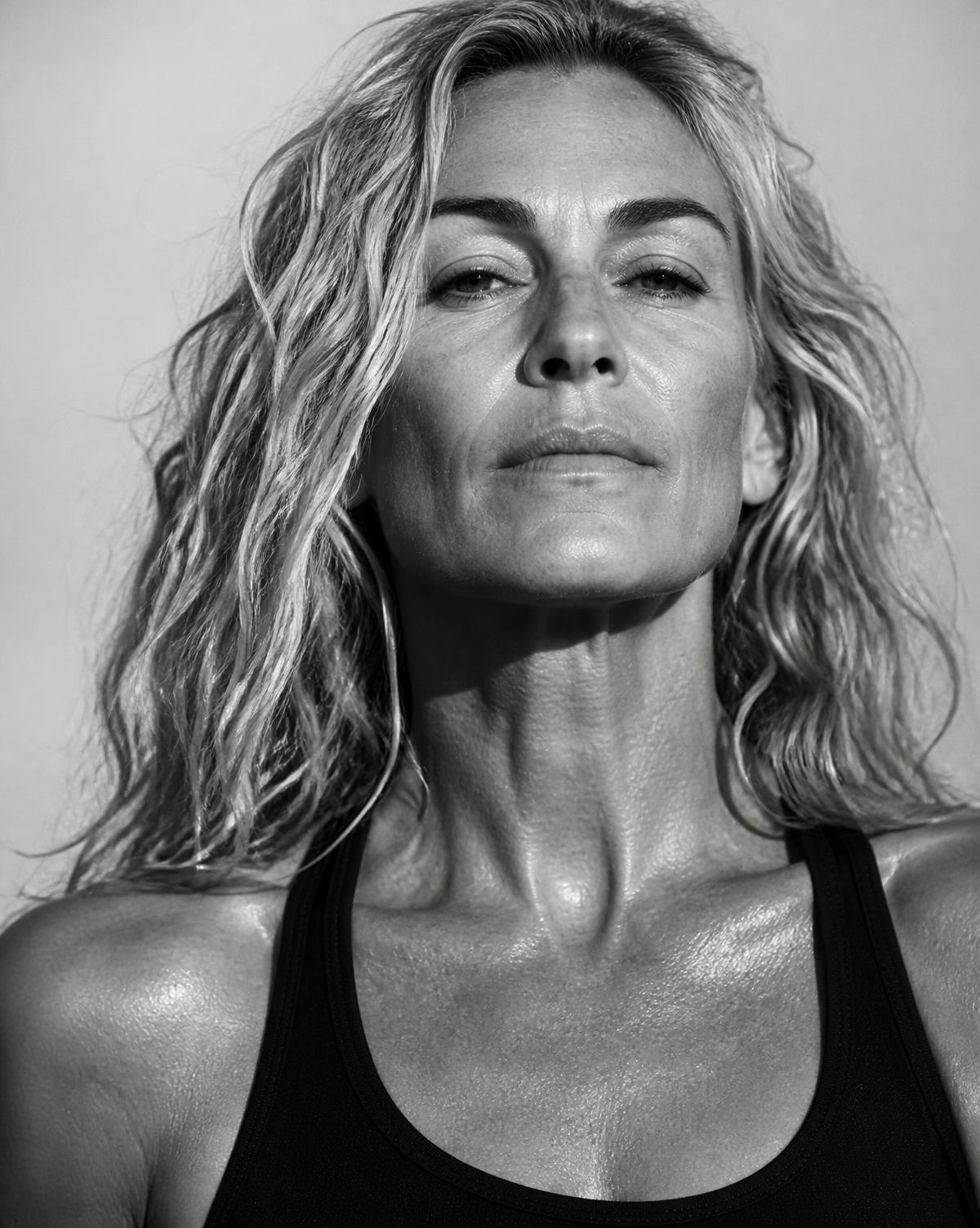 Black and white editorial portrait of a strong woman in her forties in an athletic top, fresh from a workout, looking straight at the camera